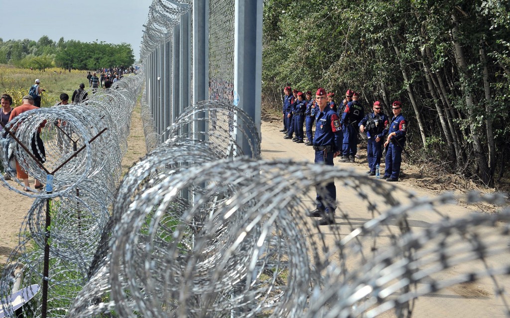 Migrants and refugees walk near razor-wire along a 3-meter-high fence secured by Hungarian police (R) at the official border crossing between Serbia and Hungary, near the northern Serbian town of Horgos on September 15, 2015. AFP PHOTO / ELVIS BARUKCICELVIS BARUKCIC/AFP/Getty Images